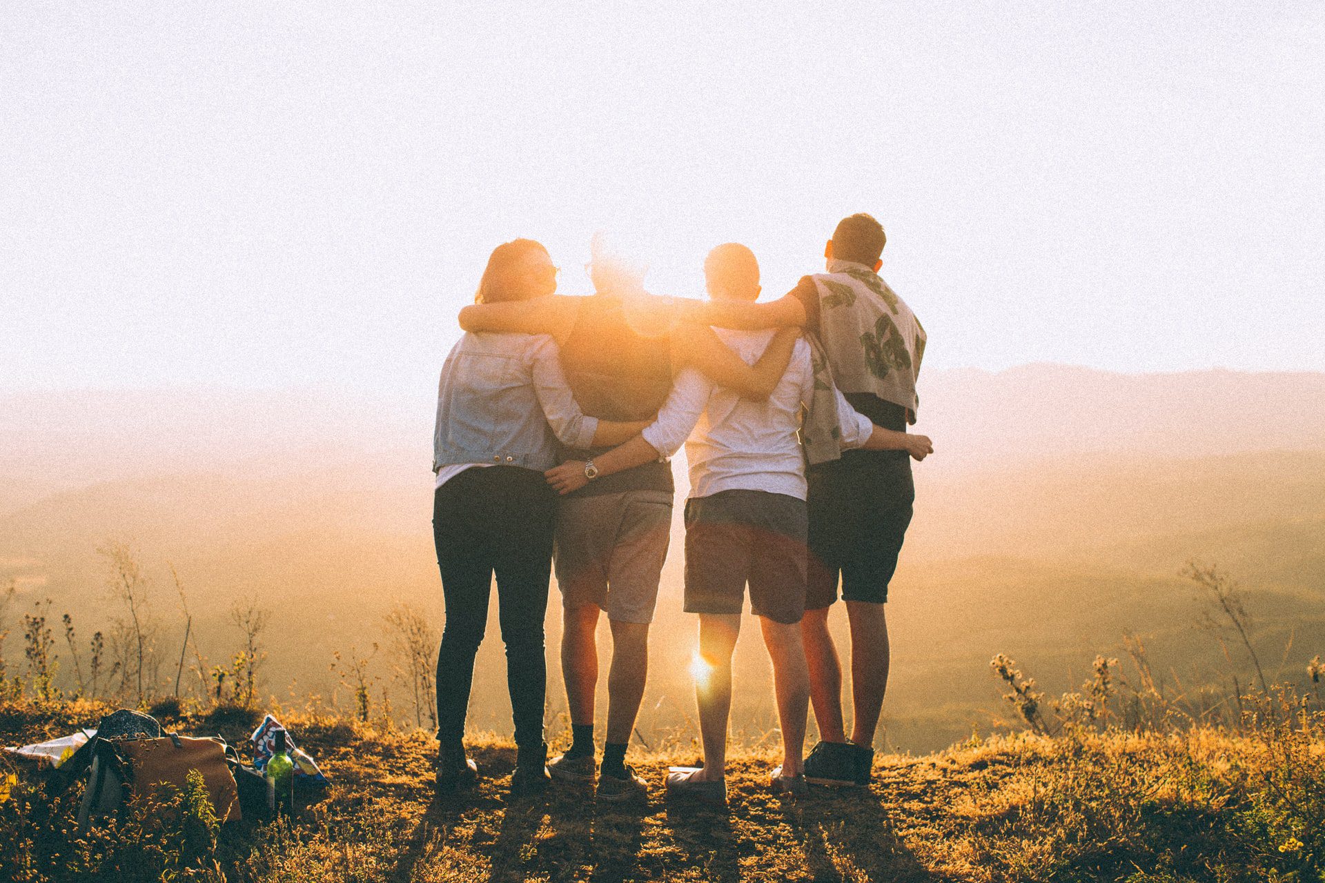 people gathered arms connected, on top of mountain, sun shining